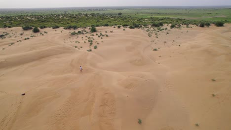 Aerial-view-of-solo-traveler-walking-on-the-sandy-dunes-of-dry-arid-desert