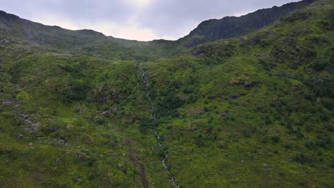 Aufsteigende-Luftaufnahme-Einer-Kaskade,-Die-über-Die-Sattelkante-Eines-Grasbewachsenen-Berges-In-Norwegen-Fließt