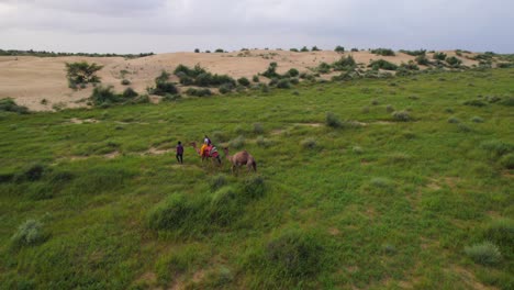 Cinematic-4K-aerial-view-of-tourist-riding-a-dromedary-through-Thar-desert-with-guide-in-private-tour