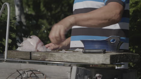Dolly-shot-of-man-preparing-and-cleans-freshly-caught-fish-on-wooden-table-outdoors