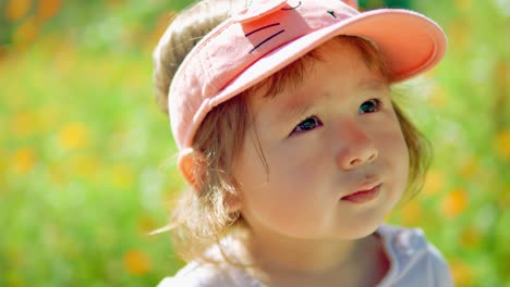 Hopeful-young-toddler-girl-looking-up-at-the-sky-and-yawning-standing-at-flower-field-in-countryside---face-close-up