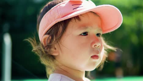 Portrait-of-little-toddler-girl-in-sport-open-top-hat-looking-aside-when-her-curly-hair-blowing-in-the-wind---face-close-up-slow-motion