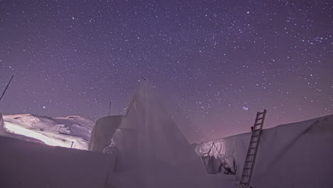 Low-angle-shot-of-star-movement-over-white-snow-landscape-with-construction-work-going-on-at-night-time-in-timelapse