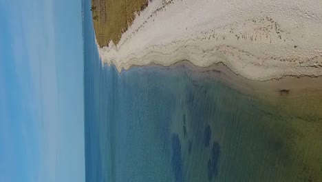 Aerial-flight-along-a-white-sands-beach-over-clear-Gulf-ocean-waters-in-vertical-format