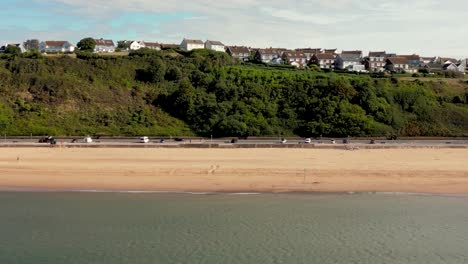 Panning-drone-shot-of-Exmouth-Beach,-Devon-from-over-the-water-showing-Marine-Drive-Promenade,-and-the-Foxhole-Hill-residential-area-on-top-of-the-cliff