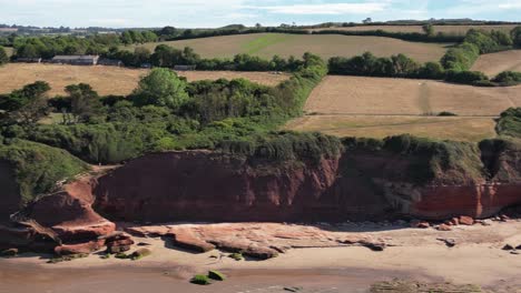Panning-Drone-shot-of-the-beach-and-red-cliffs-of-Orcombe-Point,-Exmouth-Devon-on-a-sunny-summers-morning-with-countryside-in-background