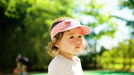 Portrait-of-pretty-toddler-girl-face-looking-aside-at-the-park-against-blurred-green-trees-on-sunny-day