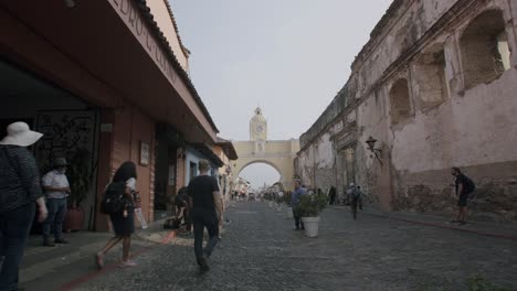 Fast-pan-down-of-the-famous-arch-in-Antigua,-Guatemala-with-people-walking-down-the-road