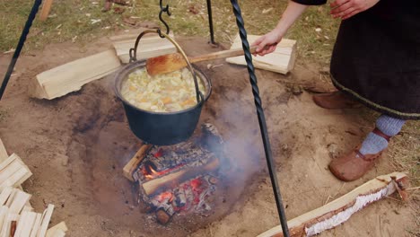 Man-with-medieval-costume-cooking-stew-in-pot-on-campfire-in-slow-motion
