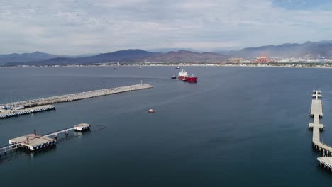 Aerial-view-of-tug-boats-assisting-an-empty-cargo-ship-to-the-Manzanillo-Port,-in-cloudy-Mexico