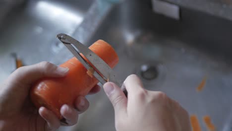 Close-up-of-hands-while-peeling-fresh-juicy-carrot-by-peeler