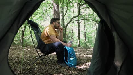 Man-eats-and-rests-sitting-on-a-chair-at-a-campsite-in-the-forest
