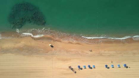 Aerial-shot-over-a-beach-of-yellow-sand-and-transparent-turquoise-water-in-Malgrat-de-Mar,-province-of-Barcelona-Flight-over-hammocks-and-deckchairs
