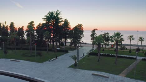 Aerial-view-of-Batumi-palm-tree-park-against-Black-sea-skyline-and-sunset,-Georgia