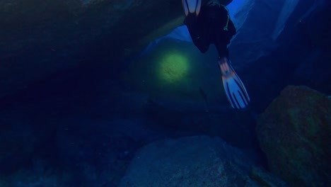 Person-is-diving-under-water-with-lamp-lightning-the-way-over-the-big-rocks