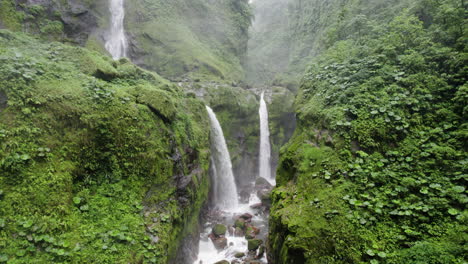 Secret-falls-cascading-into-lush-green-ravine-in-rainforest,-drone-dolly-in
