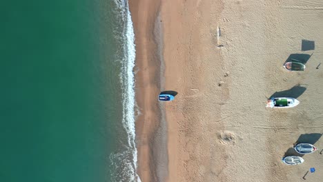 Aerial-overhead-view-of-a-beach-with-calm-turquoise-blue-waters,-fishermen-boats-in-the-foreground