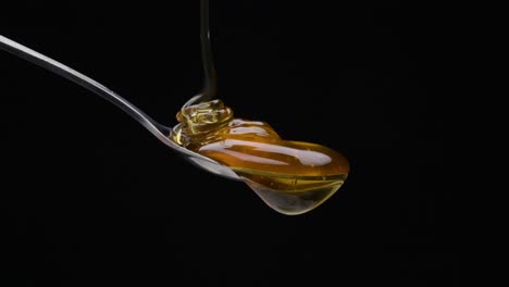 Static-shot-from-a-spoon-is-poured-over-the-honey-against-black-background