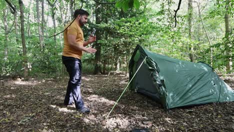 Male-traveler-successfully-finishes-setting-up-a-tent-at-the-campsite-in-the-woods-1