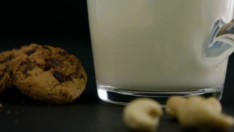 Close-up-of-a-glass-filled-with-oat-milk-on-the-side-are-cookies-and-cashew-nuts