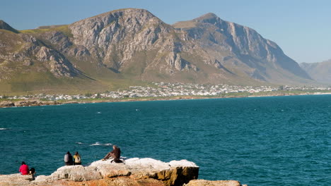 Spectators-on-coastal-rocks-whale-watching-with-beautiful-mountain-backdrop