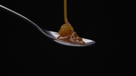 Static-shot-of-a-spoon-being-poured-over-caramel-against-black-background