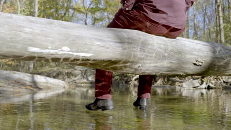 Shot-from-behind-Male-with-burgundy-clothes-sits-on-trunk-above-river,-Dolly-shot,-Loneliness-Concept