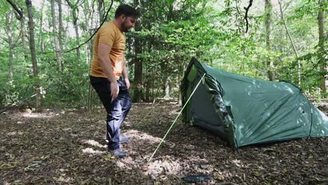 Male-traveler-successfully-finishes-setting-up-a-tent-at-the-campsite-in-the-woods