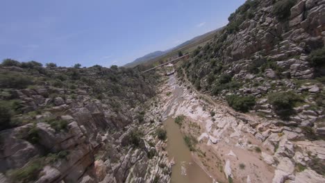 FPV-drone-flies-close-to-rugged-rock-wall-in-narrow-river-canyon-gorge