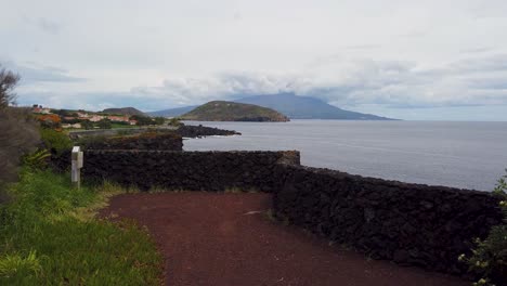 Revealing-landscape-in-Azores,-Faial-Island,-with-ocean-hitting-shore-and-mountains-in-the-background
