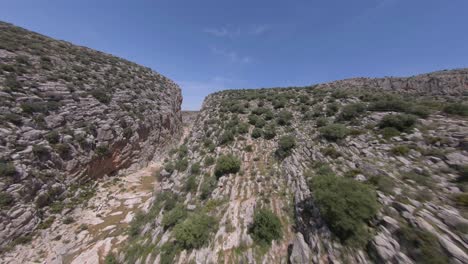 Low-FPV-aerial-along-arid,-rugged-rock-canyon-rim-leads-to-dive-inside