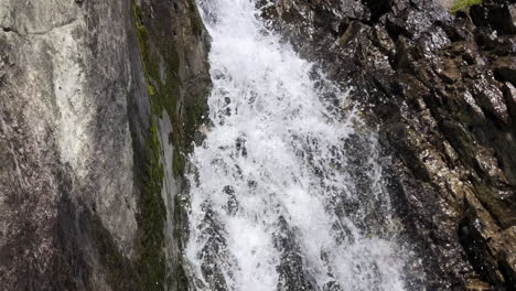 Small-waterfall-in-between-rocks-in-the-swiss-alps,-fresh-water-from-the-glacier-in-the-mountain