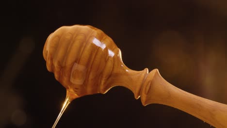 Static-shot-of-rotating-honey-spoon-with-delicious-dripping-honey-against-black-background