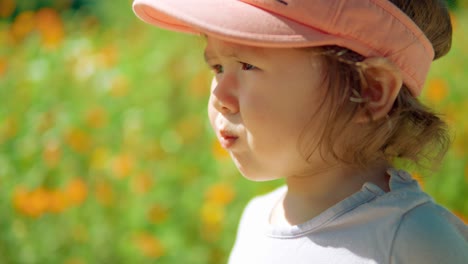 Portrait-of-pretty-toddler-girl-chewing-gum-or-snack-at-the-flowering-meadow