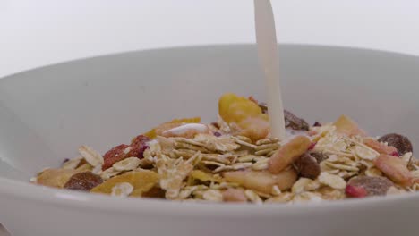 Close-up-of-a-white-spinning-bowl-against-white-background-filled-with-vegan-cereal-with-fruits-being-poured-into-the-vegan-oat-milk-for-breakfast