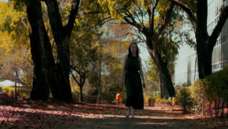 Handheld-shot-of-confident-woman-in-green-dress-walking-in-park-towards-camera