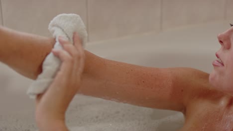Beautiful-woman-relaxing-in-bath-using-a-washcloth-to-clean-her-arm