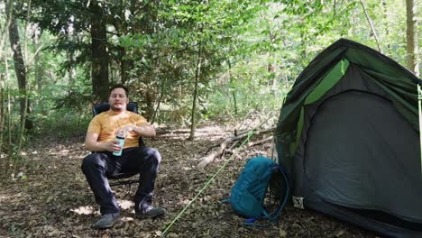 Tired-and-exhausted-man-sits-on-a-chair-in-front-of-a-tent-to-rest-and-drink-water