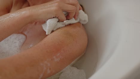 Attractive-woman-relaxing-in-bath-scrubbing-her-arm-with-washcloth