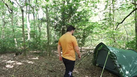 Man-going-to-a-tent-at-campsite-in-the-woods-and-crouches-down-in-front-of-the-entrance