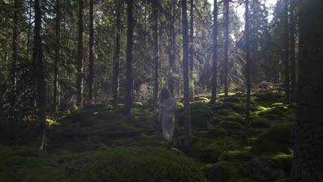 Rear-view-of-young-girl-wonder-lost-in-mossy-deep-forest,-light-shining-through