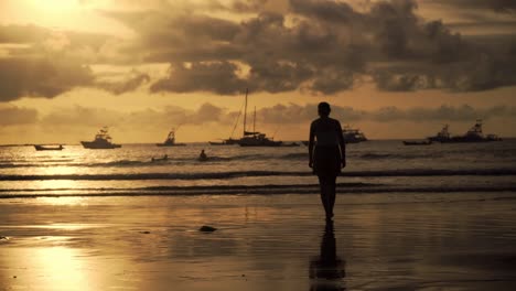 Frau-Silhouette-Zu-Fuß-An-Einem-Strand-In-Tamarindo-In-Costa-Rica-Mit-Booten-Im-Hintergrund