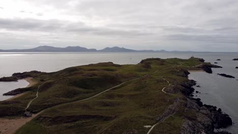 Aerial-reversing-view-Ynys-Llanddwyn-island-Anglesey-coastal-walking-trail-with-Snowdonia-mountains-across-the-Irish-sea