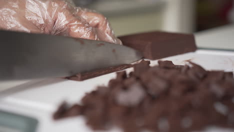 Hand-In-Disposable-Glove-Chopping-Dark-Chocolate-Bar-On-Cutting-Board