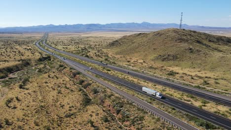 Aerial-view,-Cars-Trucks,-Semis-Driving-on-highway,-Mountains-and-Cell-Tower-in-Background