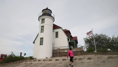 Woman-walking-near-historic-Point-Betsie-Lighthouse-in-Frankfort,-Michigan-along-Lake-Michigan-with-gimbal-video-from-behind