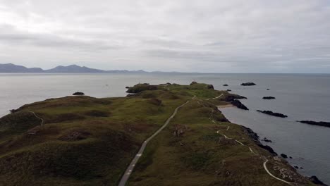 Aerial-view-Ynys-Llanddwyn-island-Anglesey-coastal-walking-trail-with-Snowdonia-mountains-across-the-Irish-sea-pull-back