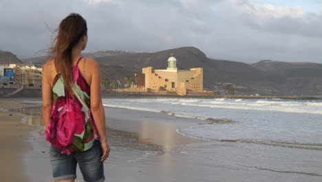 Cinematic-shot-of-a-woman-admiring-the-Alfredo-Kraus-auditorium-from-Las-Canteras-beach,-on-the-island-of-Gran-Canaria-1