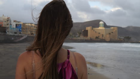 Close-up-cinematic-shot-of-a-woman-walking-and-admiring-the-Alfredo-Kraus-auditorium-from-Las-Canteras-beach,-on-the-island-of-Gran-Canaria
