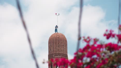A-man-is-trying-to-install-copper-crescent-on-the-top-of-the-minaret-through-the-power-cables-and-red-flowers